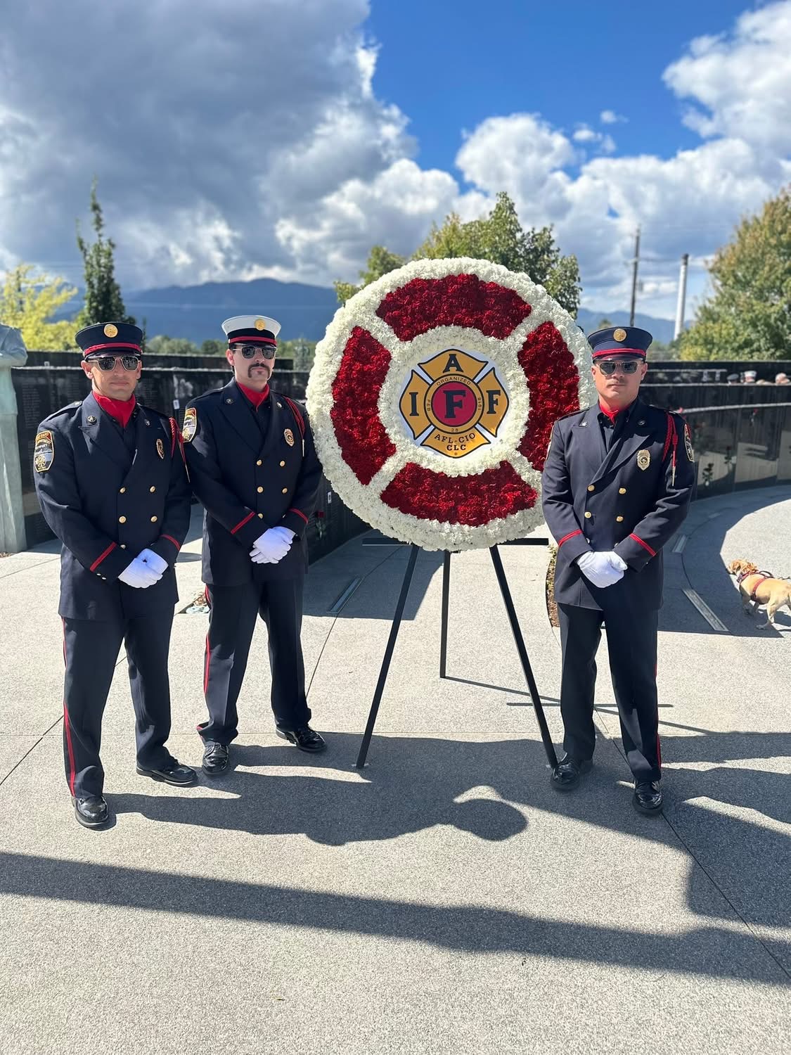 Three Katy Honor Guard members standing beside an IAFF memorial wreath at a remembrance site