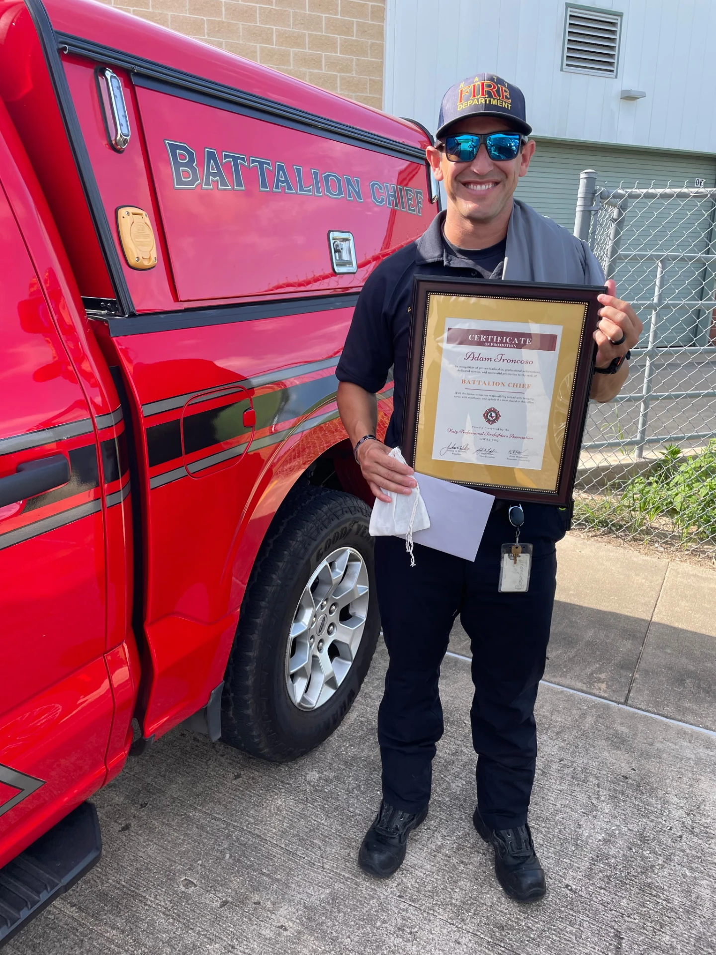 Fire department member holding a framed certificate beside a marked vehicle